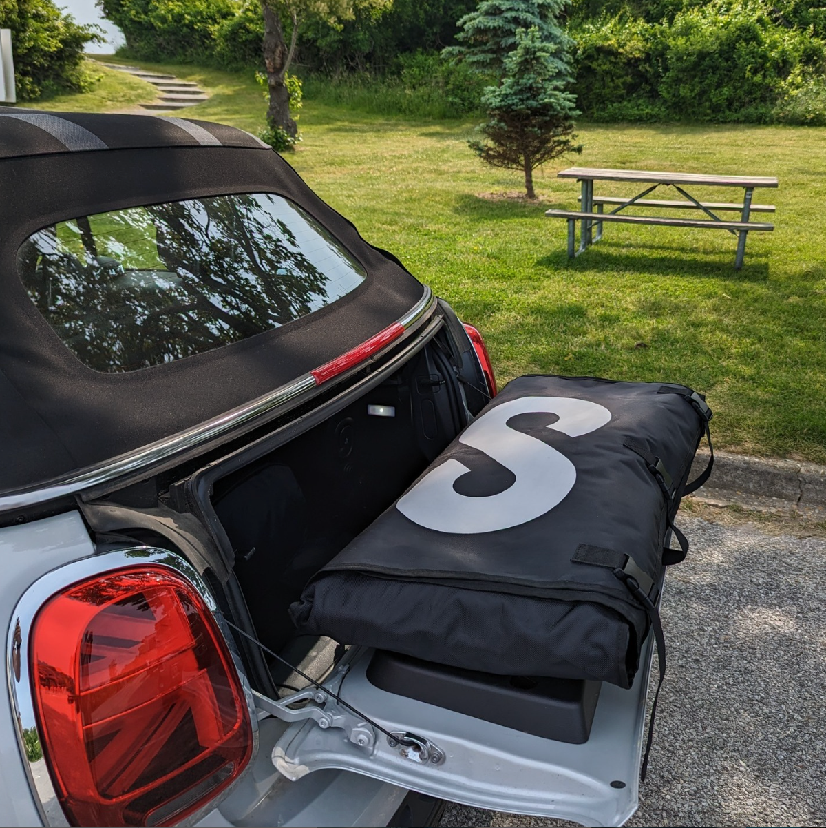 A Sipaboards in a backpack sitting on the trunk lid of a gray mini cooper.