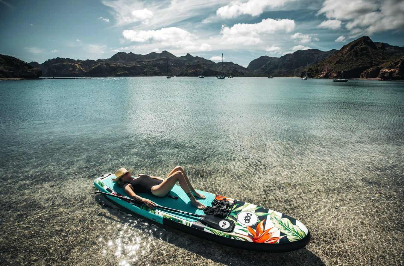 Girl laying on inflatable paddle board in shallow water.