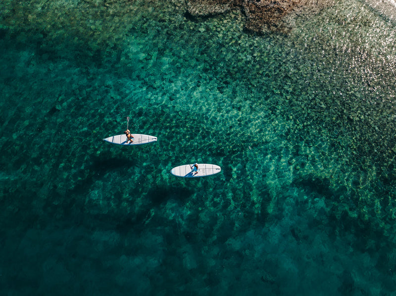 Two paddle boarders in tropical green water from above. 