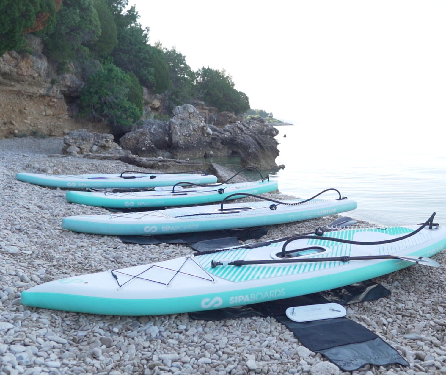 Four SipaBoards Drive Tourer Aqua Paddle Boards inlfated on a beach next to the water.