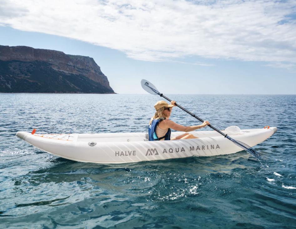 Girl paddling Aqua Marina Halve Inflatable Kayak out in the water, with a rocky coastline in the background.