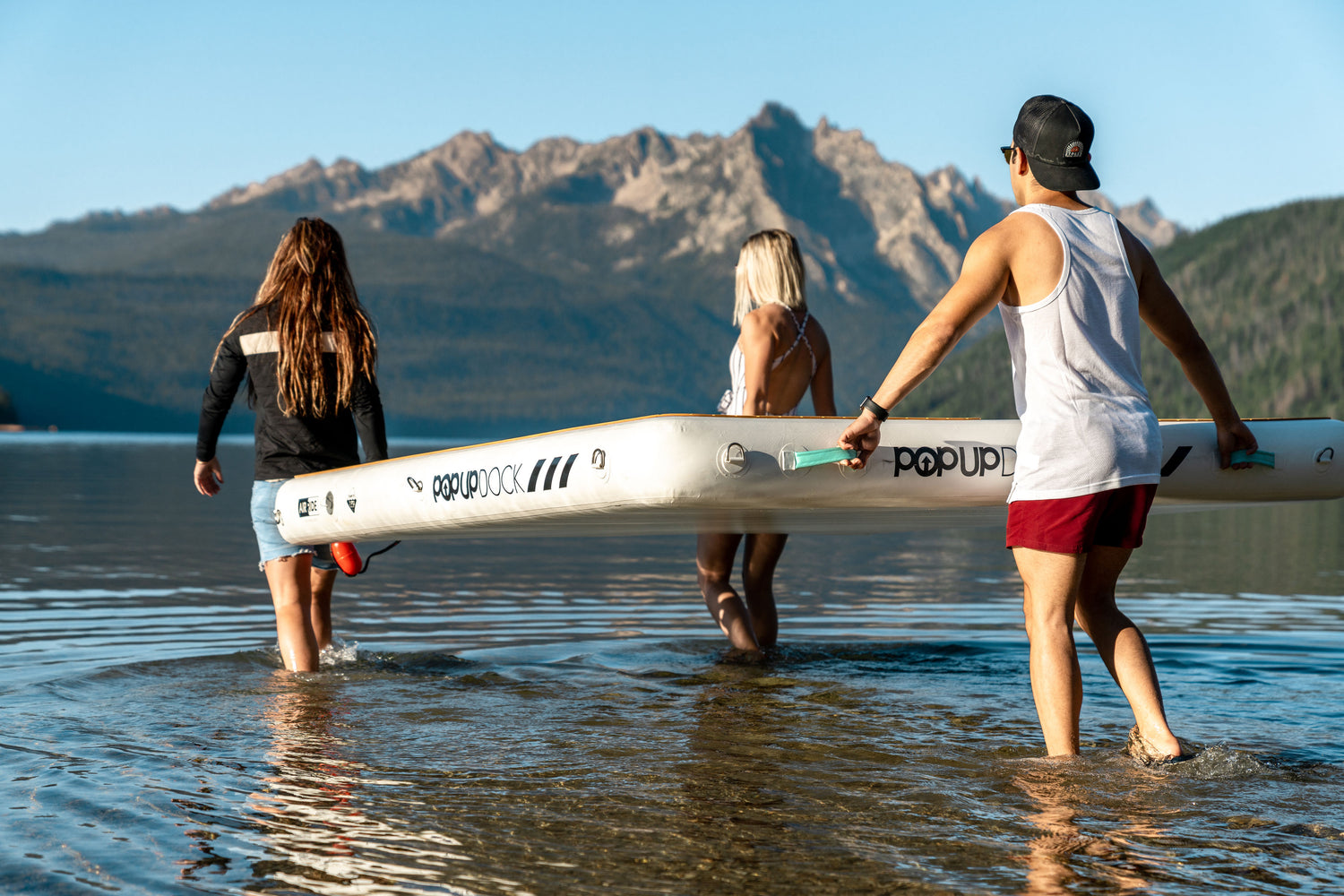 A boy with two girls carrying an inflated POPUP Dock 8x7 Inflatable Platform to the water.