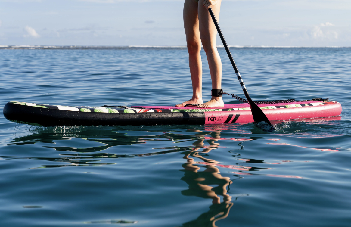 Person on inflatable stand up paddle board in water, shot from the waist down. 