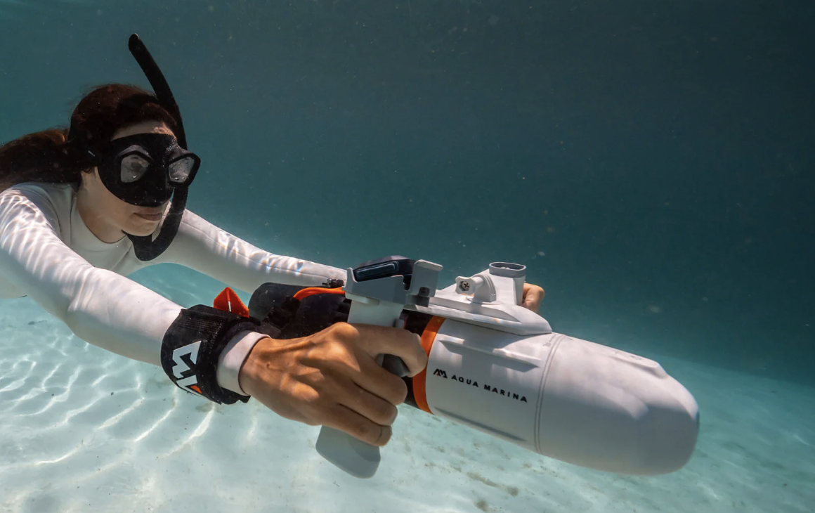 Girl with snorkel on underwater, arms extended, riding behind Blue Drive Underwater sSea Scooter from Aqua Marina, which she is steering.