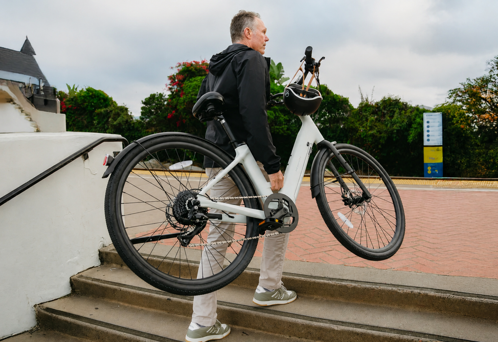 Man carrying a lightweight carbon fiber frame Urtopia Carbon Classic ST eBike up the stairs to a pavered walkway.
