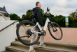 Man carrying a lightweight carbon fiber frame Urtopia Carbon Classic ST eBike up the stairs to a pavered walkway.