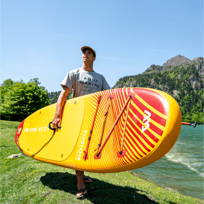 Guy carrying Aqua Marina Fusion SUP near water. 