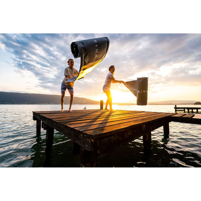 Two Aqua Marina Glow SUPs unrolled in air, on a dock at sunset.