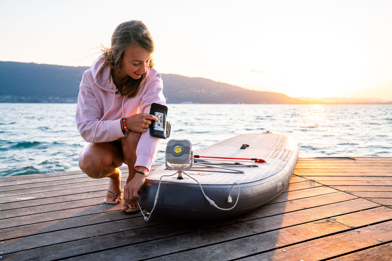 Girl on a wood dock programing the lights on her Aqua Marina Glow Inflatable SUP using the included remote control.