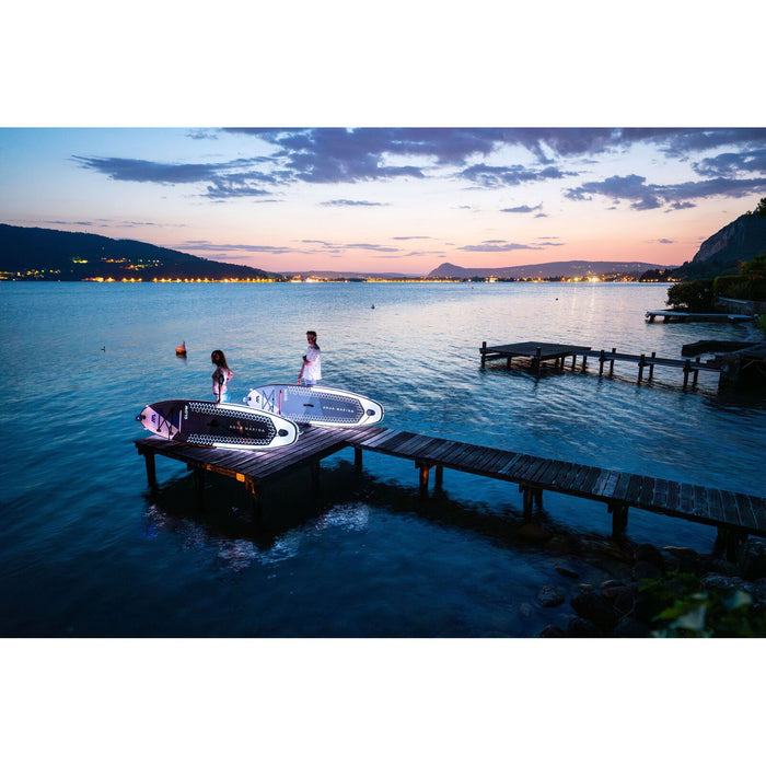 Two Aqua Marina Glow SUPs illuminated with paddle boarders standing on dock at night.