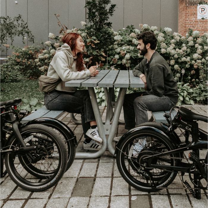 CARBO Model S Electric Bike couple at table next to folded bikes.