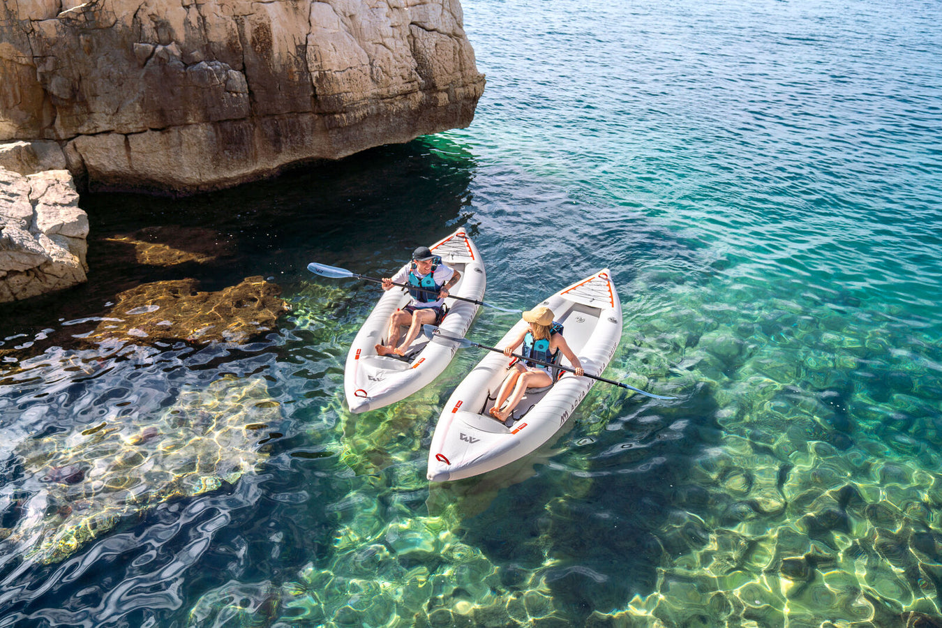 Couple in two inflatable kayaks in tropical water near rock formation coastline. 