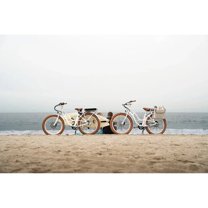 Couple sitting on a beach with two Priority E-Coast electric bikes behind them. 