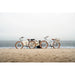 Couple sitting on a beach with two Priority E-Coast electric bikes behind them. 