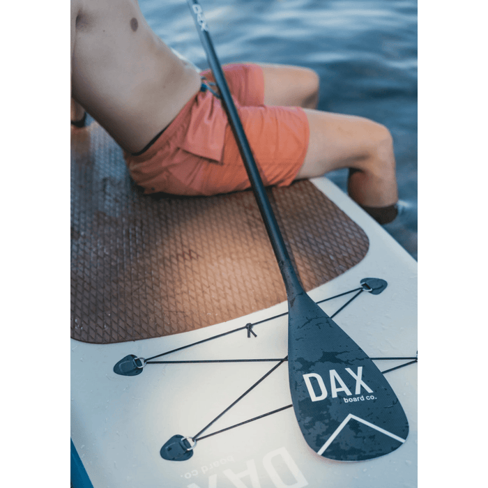 Guy from check down sitting on a Dax Board Co. Air High Tide iSUP on the water with a paddle across his lap.