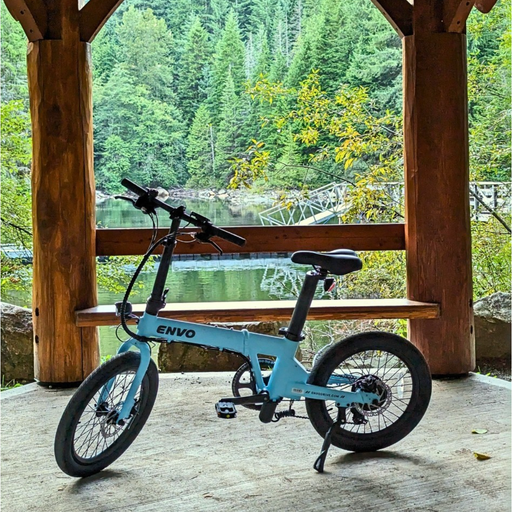 Baby blue ENVO Lynx eBike parked in wooden pavilion with water and forestry in the background.