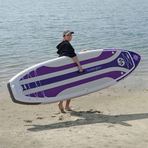 Girl in a hat carrying a purple NIXY Huntington G5 iSUP down the beach.