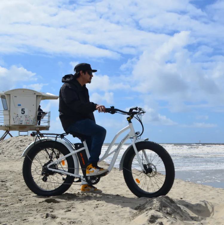 Guy on electric bike looking over coast with lifeguard station behind him.