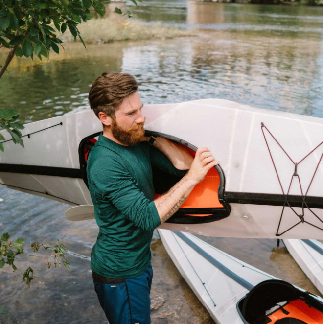 Guy carrying an Oru Kayak Bay ST to the water showing it's bungee systems.