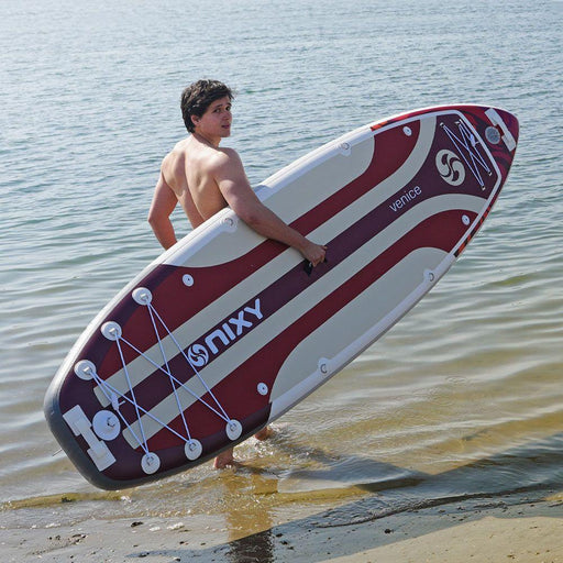 Guy carrying a red NIXY Venice G5 Inflatable SUP into murky water.