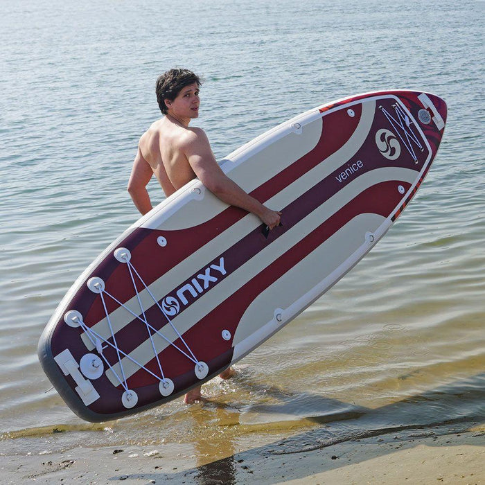 Guy carrying a red NIXY Venice G5 Inflatable SUP into murky water.