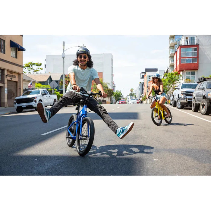 Guy in the middle of the street having fun on his blue JackRabbit OG2 with his girlfriend riding her yellow one behind him.