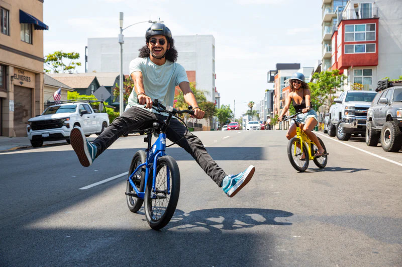 Guy in the middle of the street having fun on his blue JackRabbit OG2 with his girlfriend riding her yellow one behind him.