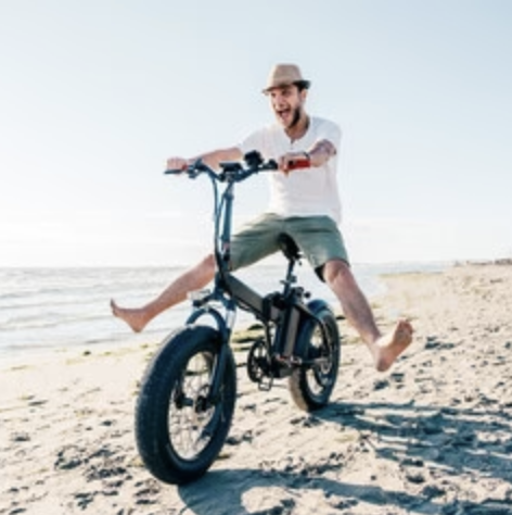 Guy riding E-Bike on beach with legs off pedals.