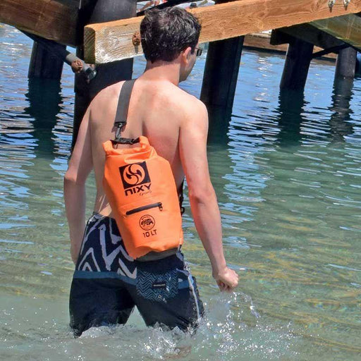 Guy walking into the water using the NIXY Orange Dry Bag.