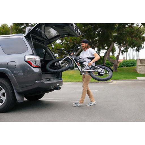 Man carrying JackRabbit MG Renegade electric bicycle out of an open SUV trunk on a street.