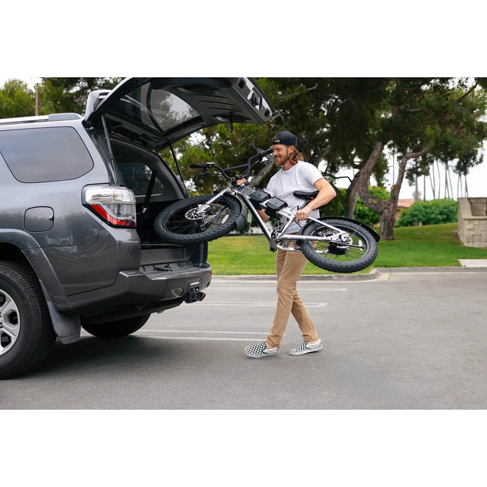 Man carrying JackRabbit MG Renegade electric bicycle out of an open SUV trunk on a street.