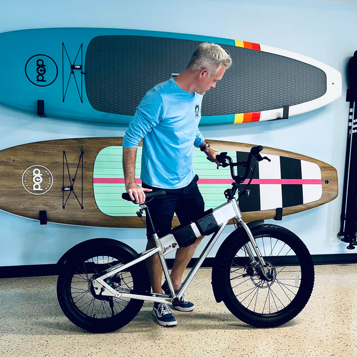Guy standing with a Silver JackRabbit Renegae eBike with POP Board Co. SUP's behind him on the wall in Fort Myers Beach.
