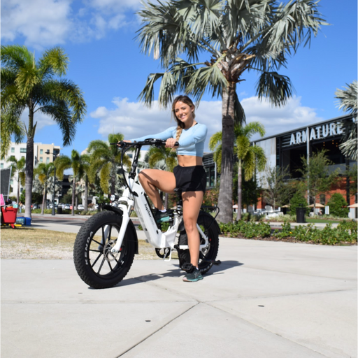 Girl with a braid posing on a white Jupiter Defiant ST Foldable Fat Tire Electric Bike with palm trees in the background.