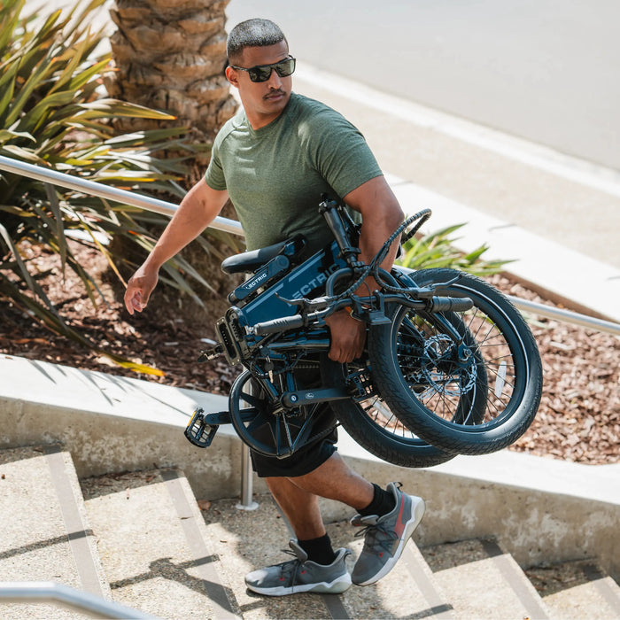 Guy carring folded Lectric XP Lite eBike up stairs.