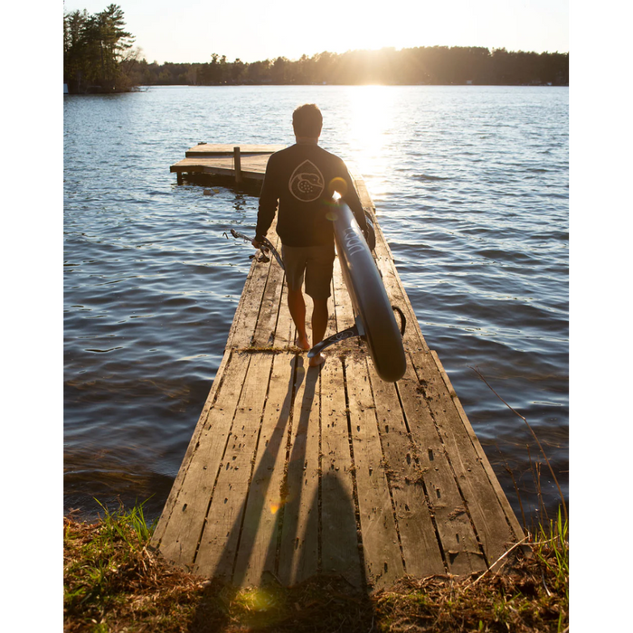 Guy carrying an inflated Loon REALTREE Fishing SUP down a dock to the water at sunset.