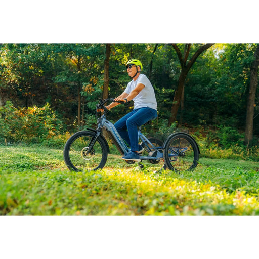 Man riding a blue Denago Trike 1 on a trail with greenery.