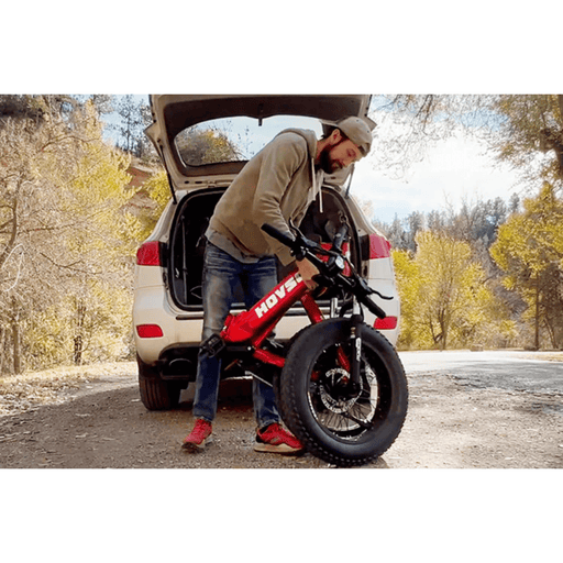 Man picking up a folded red HOVSCO HovBeta Electric Bike to put in the back of his vehicle.