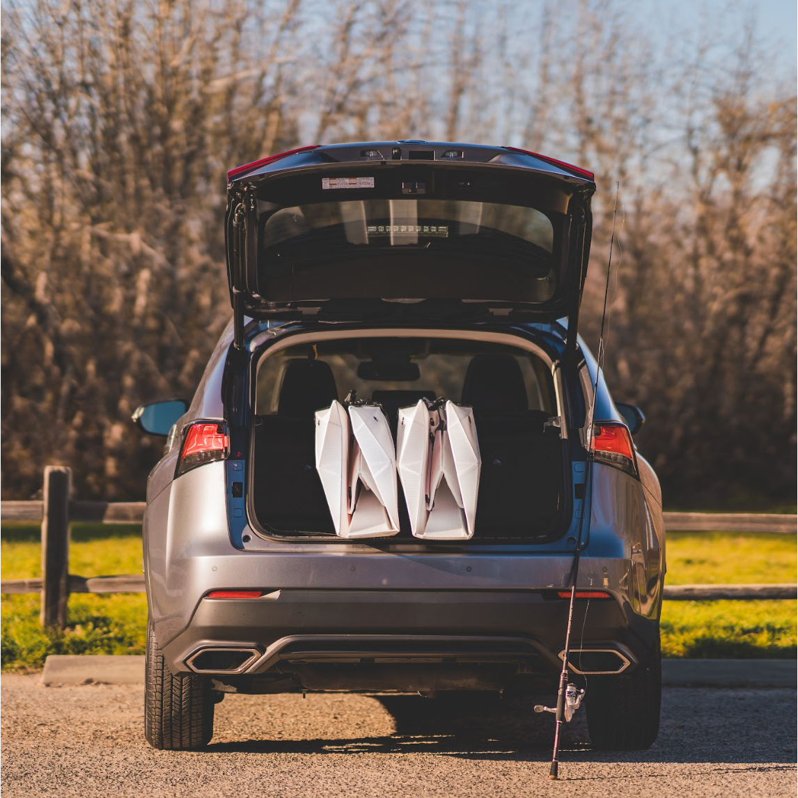 Two Oru Lake Kayaks folded and packed in back of car with fishing pole leaning against car.