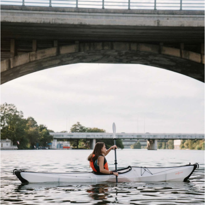Girl paddling a white Oru Bay ST Kayak under a bridge.