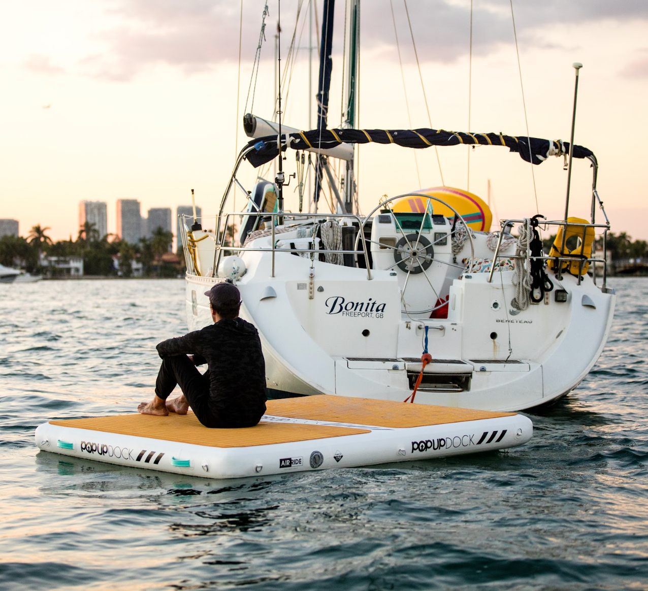 Guy sitting on POP Board Co. POPUP Dock behind sailboat around sunset.