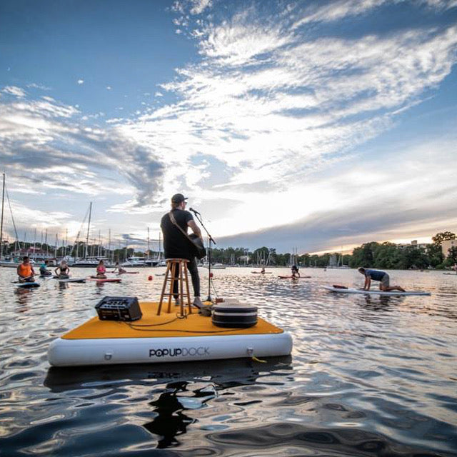 POP Board Co. POPUP Dock with guy playing music on it to paddle boarders on the water. 