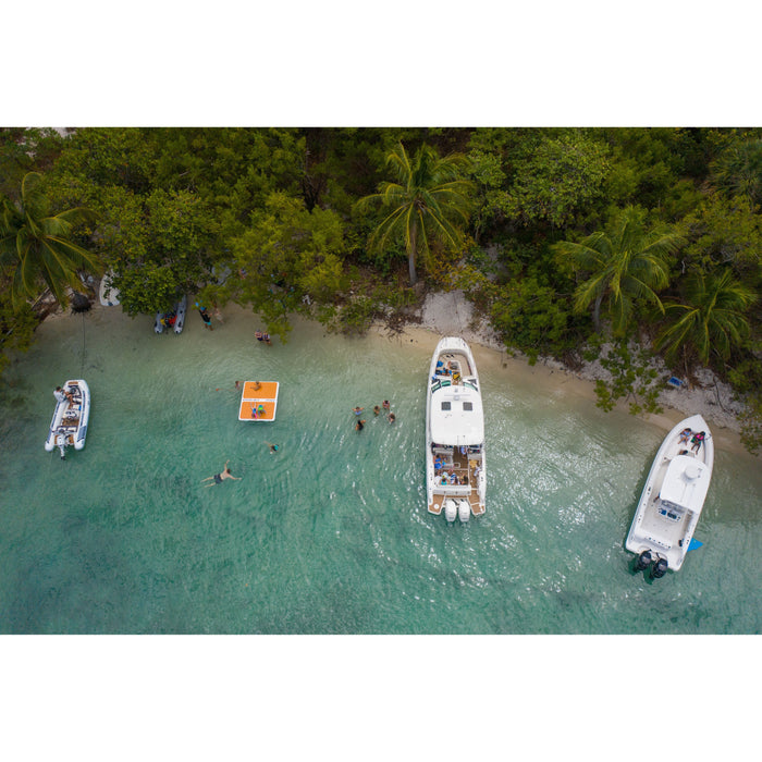 The POPUP Dock 8x7 Inflatable Platform floating off a tropical beach with boats on each side.