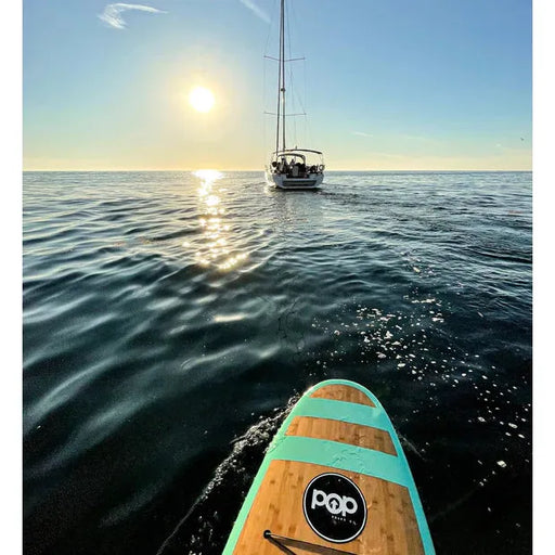 11' Huckleberry paddleboard from POP Board Co. on the water behind a sailboat.