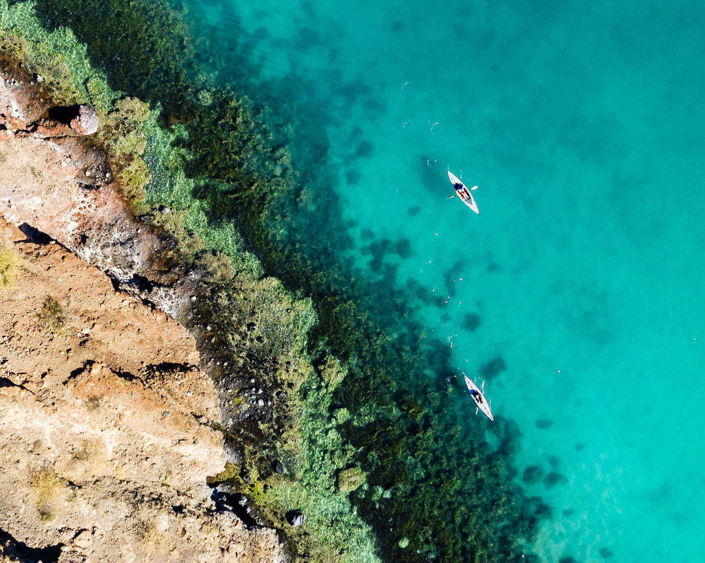 Two foldable kayaks in tropical water near rocky coastline.