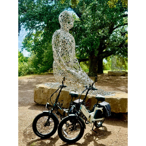 Two XP4 electric bikes parked in front of a wire sculpture of a person sitting outdoors.