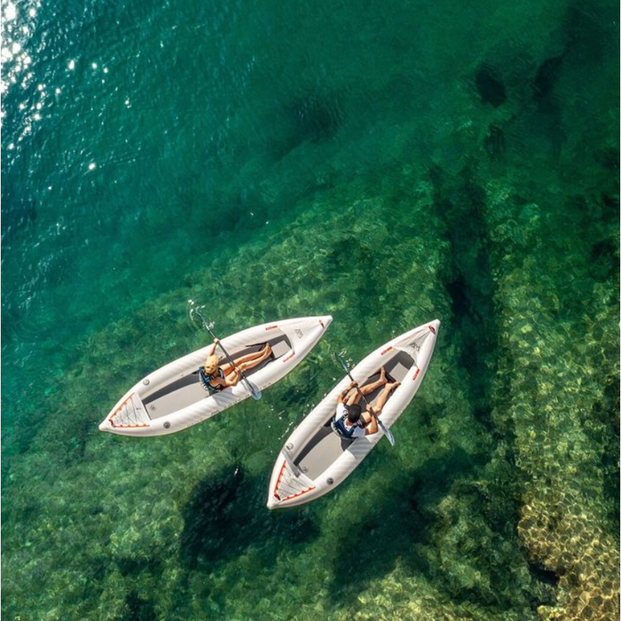 Two people in separate Aqua Marina Halve Kayaks floating in shallow water with paddles across their laps.
