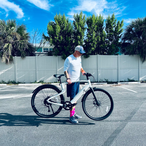 Guy picking up Urtopia Carbon Pro 1 lightweight electric bike in a parking lot with trees and a blue sky in the background.