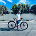 Guy picking up Urtopia Carbon Pro 1 lightweight electric bike in a parking lot with trees and a blue sky in the background.