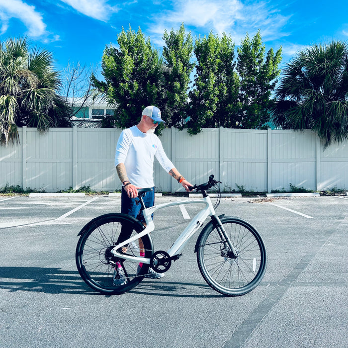Man standing behind a Urtopia Carbon 1 Pro eBike in a parking lot with trees and a fence in the background.