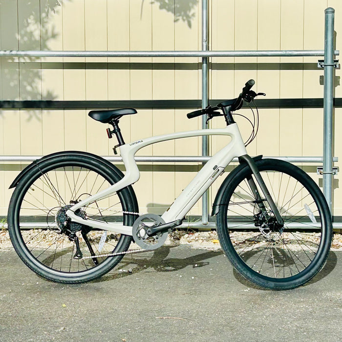 Urtopia Carbon 1 Pro eBike parked on a sidewalk with a tan gate in the background.